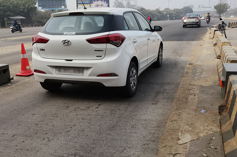 A white car driving past the Opus Remote Sensing device in Delhi, India.